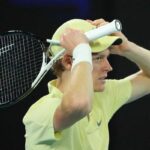 Jannik Sinner di profilo e con le mani sul cappellino