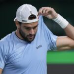 Matteo Berrettini pensieroso si tira su la maglia con una mano