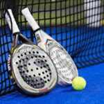 Due racchette da padel appoggiate alla rete e una pallina