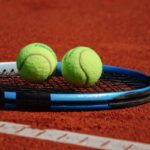 Racchetta e due palline da tennis appoggiate sulla terra rossa